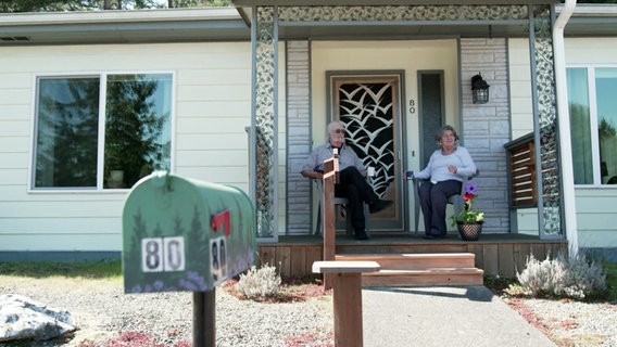 Ein älterer Herr und eine ältere Frau sitzen auf einer kleinen Veranda. © Screenshot 