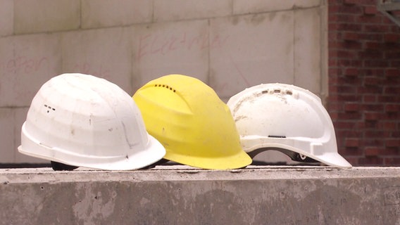 Drei Helme liegen auf einer Mauer auf einer Baustelle. © Screenshot 