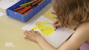 Ein Kind zeichnet mit Buntstiften eine gelbe Figur. © Screenshot 