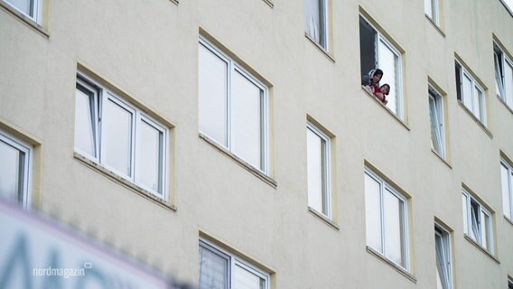 Eine Frau mit Kopftuch und ein kleines Kind schauen aus dem Fenster eines großen Gebäudes. © Screenshot 