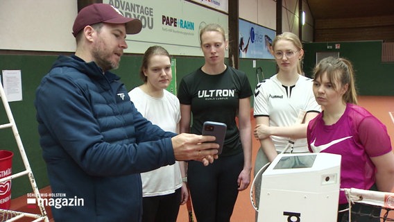 Trainer und Spielerinnen schauhen auf ein Smartphone. © Screenshot 