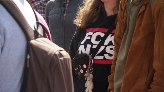 Nahaufnahme von einer Frau, die ein Oberteil trägt mit der Aufschrift "FCK NZS". © Screenshot 