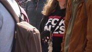 Nahaufnahme von einer Frau, die ein Oberteil trägt mit der Aufschrift "FCK NZS". © Screenshot 