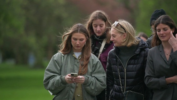 Junge Frauen gehen spazieren. Eine schaut gerade auf ihr Smartphone. © Screenshot 