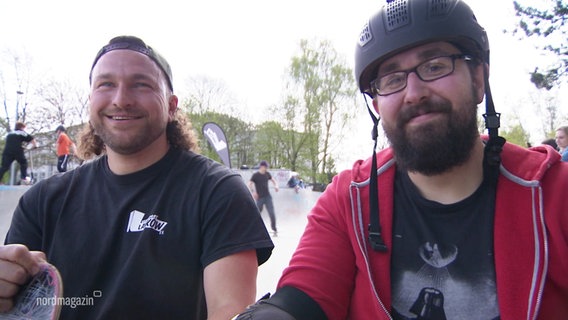 Reporter Chris Loose (rechts) lächelt in die Kamera. Er trägt einen Fahrradhelm. Neben ihm sitzt Skate-Coach Roland. © Screenshot 
