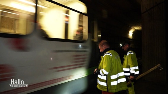 Zwei Üstra Mitarbeiter bei einer Inspektion im Stadtbahntunnel stehen vor einem vorbefahrenden Zug. © Screenshot 