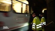 Zwei Üstra Mitarbeiter bei einer Inspektion im Stadtbahntunnel stehen vor einem vorbefahrenden Zug. © Screenshot 