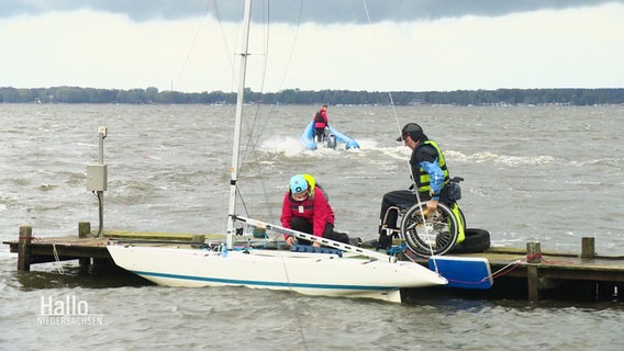 Auf einem Steg steigen Menschen mit und ohne Rollstuhl in ein Segelboot ein. © Screenshot 
