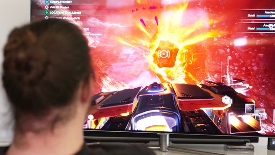 Ein Mann sitzt vor einem Bildschirm auf dem eine Szene eines Computerspiels zu sehen ist. © Screenshot 