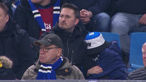 Einige Fußball-Fans schauen enttäuscht auf das Spielfeld. © Screenshot 