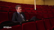 Gabriel Feltz, zukünftiger Generalmusikdirektor in Kiel, sitzt in einem Zuschauersitz, bezogen mit rotem Samt. © Screenshot 