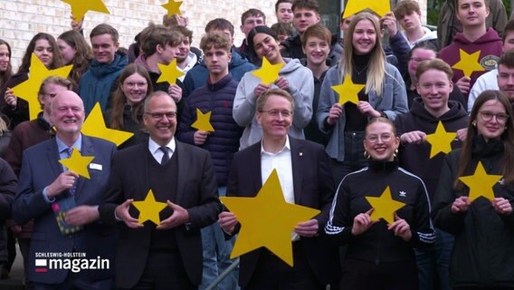 Junge Menschen und der Ministerpräsident von Schleswig-Holstein, Daniel Günther, stehen auf einer Treppe und halten gelbe Europa-Sterne. © Screenshot 