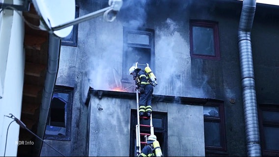 Feuerwehrleute bei der Arbeit an einer verrußten Außenwand eines Gebäudes. © Screenshot 