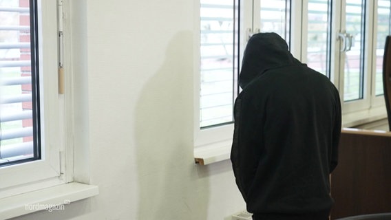 Ein Angeklagter trägt einen schwarzen Hoodie über dem Kopf. © Screenshot 
