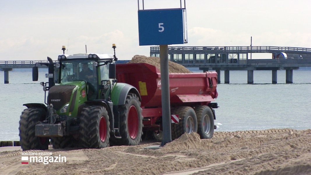 Ein Traktor fährt mit einer Ladung Sand am Strand entlang.