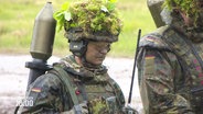 Soldaten in Tarn- und Schutzkleidung sowie mit Moos und Zweigen getarnten Helmen. © Screenshot 