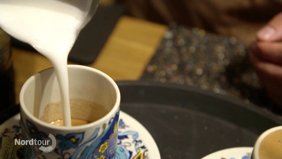 Aufgeschäumte Milch wird in eine geblümte Kaffeetasse gegossen. © Screenshot 