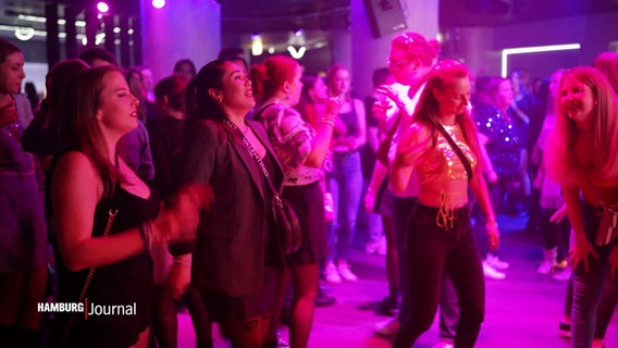 Junge Frauen tanzen in violettem Licht zu Taylor Swift Musik. © Screenshot 