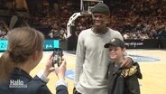 Der NBA-Star Dennis Schröder lässt sich mit einem Fan fotografieren. © Screenshot 