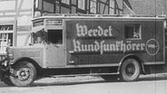 Histprisches Schwarz-Weiß-Bild: Ein Lkw mit der Aufschrift "Werdet Rundfunkhörer" fährt durch eine Straße © Screenshot 