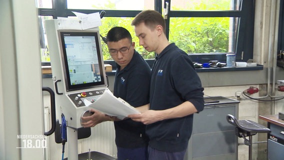 Zwei junge Männer stehen in einem Handwerksbetrieb an einer Maschine. © Screenshot 