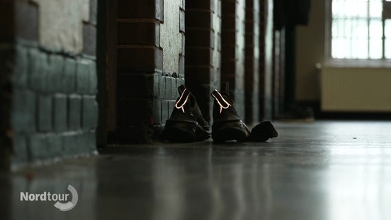 Schuhe von einem Inhaftierten stehen auf dem Fußboden vor der Zelle. © Screenshot 