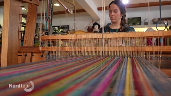 Textildesignerin Linda Detering sitzt an einem traditionellen Webstuhl. © Screenshot 