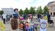 Eltern und Kinder bereiten sich vor auf eine Fahrrad-Demonstration und ziehen Fahrradhelme an. © Screenshot 
