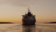 Ein Containerschiff fährt die Elbe entlang, man sieht es im Abendlicht von achtern. © Screenshot 