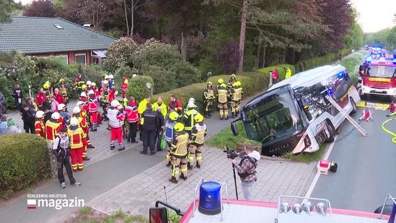Szene am Unfallort: Ein Linienbus liegt im Graben, Polizeibeamte und Feuerwehrleute im Einsatz. Eine Anstellleiter lehnt an einem zerschlagenen Fenster des Busses. © Screenshot 