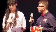 Zwei Gewinner*innen des 21 FISH Filmfestivals stehen auf einer Bühne und nehmen ihre Preise entgegen. © Screenshot 