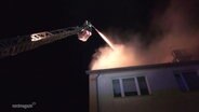 Ein Feuerwehrmann löscht aus einem Leiterwagen heraus ein Feuer im Dach eines Wohnhauses. © Screenshot 