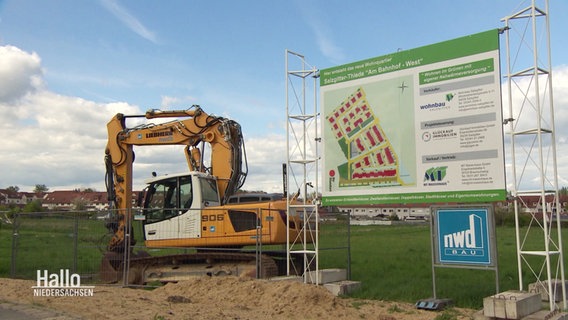 Ein Bagger steht an einer Baustelle, ein Schild weist auf eine geplante Neubau-Siedlung hin. © Screenshot 
