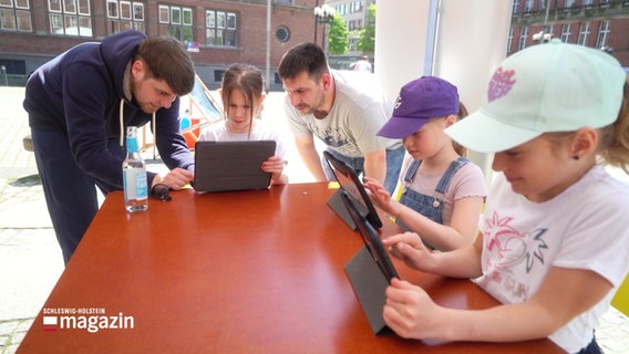 Mehrere Kinder sitzen an einem Tisch und schauen auf Tablets. © Screenshot 