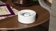 Auf einem Tisch steht ein weißer Plastik-Aschenbecher. © Screenshot 