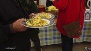 Ein Mann hält zwei Teller mit asiatischen Gerichten in den Händen. © Screenshot 