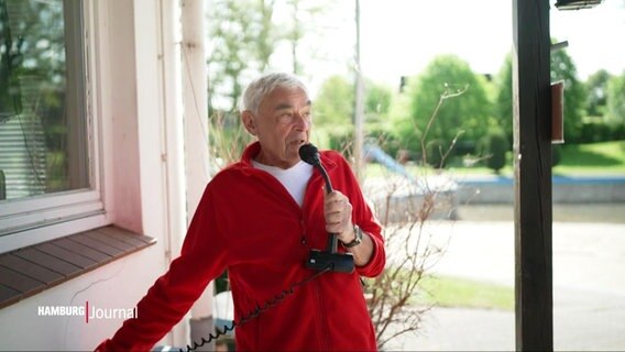 Ein Mann im roten Pullover redet in ein Mikrofon. © Screenshot 