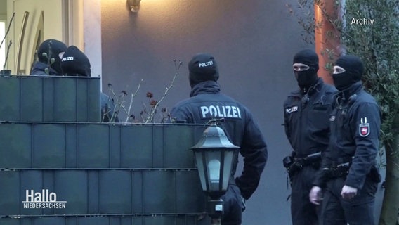 Polizistinnen und Ploizisten stehen mit Sturmhauben vor einem Haus. © Screenshot 