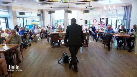 Infoveranstaltung der Initiative gegen gerndern. Ein Redner spricht vor einem Publikum aus voriwegend älteren Menschen. © Screenshot 