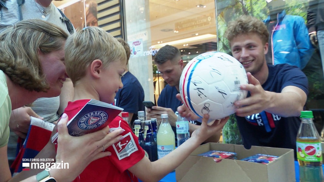Ein kleiner Junge freut sich über den handsignierten Fußball seiner Kieler Lieblingsmannschaft.