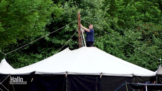 Eine Person auf einer Leiter am Dach eines großes Zeltes. © Screenshot 