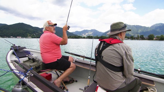 Heinz Galling und Horst Henning sitzen in einem Boot auf einem Bergsee vor Alpenpanorama und angeln. © Screenshot 