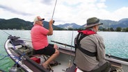 Heinz Galling und Horst Henning sitzen in einem Boot auf einem Bergsee vor Alpenpanorama und angeln. © Screenshot 