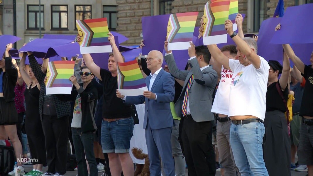 Eine Gruppe Menschen mit Regenbogenfahnen vor dem Hamburger Rathaus, darunter Bürgermeister Peter Tschentscher.
