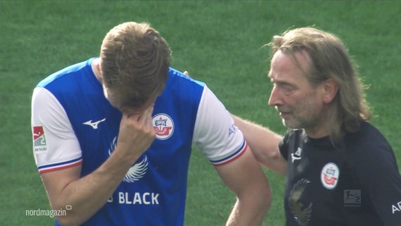 Ein Spieler von Hansa Rostock vergräbt sein Gesicht in der Hand, ein Kollege legt ihm verständnisvoll eine Hand auf den Rücken. © Screenshot 