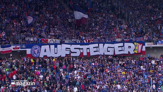 Holstein Kiel Fans halten in einem Stadion ein Banner mit der Aufschrift: "Aufsteiger". © Screenshot 