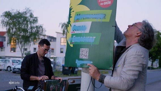 Zwei Männer entfernen ein Wahlplakat der Grünen, welches mit blauer Farbe beschmiert wurde. © Screenshot 