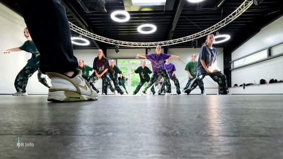 Blick vom Fußboden eines Tanzstudios auf eine Gruppe junger HipHop-Tänzerinnen, die in Formation tanzen. © Screenshot 