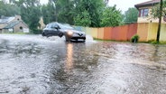 Ein Auto fährt im Regen über eine stark überschwemmte Straße. © Screenshot 
