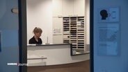 Eine Ärztin sitzt am Empfang ihrer Gemeinschaftspraxis. © Screenshot 